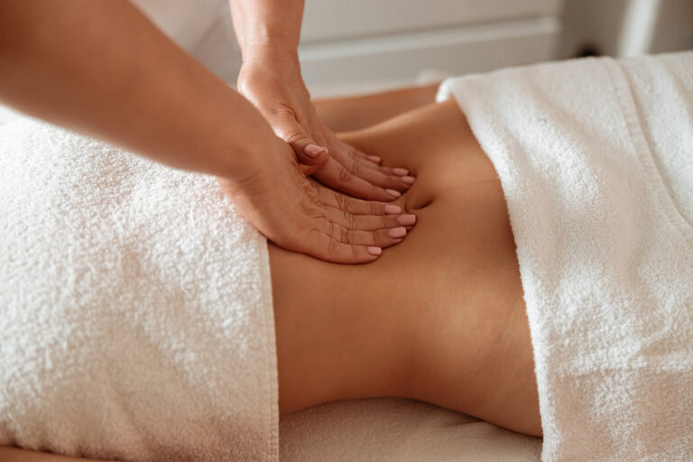 Masseuse massaging female client abdomen in spa salon